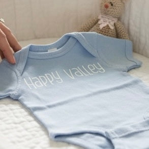Blue baby onesie with 'Happy Valley' text on a white surface.