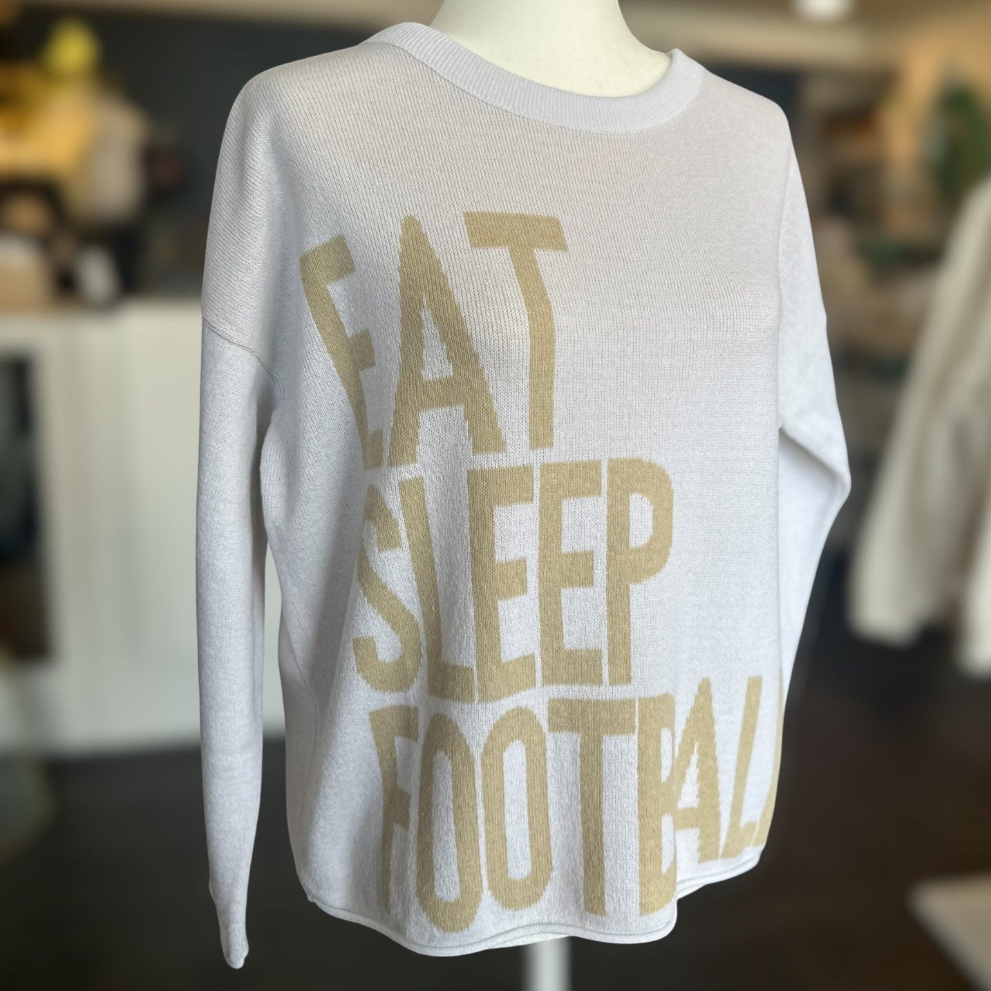 White sweatshirt with 'Eat Sleep Football' text on a mannequin in a store setting.
