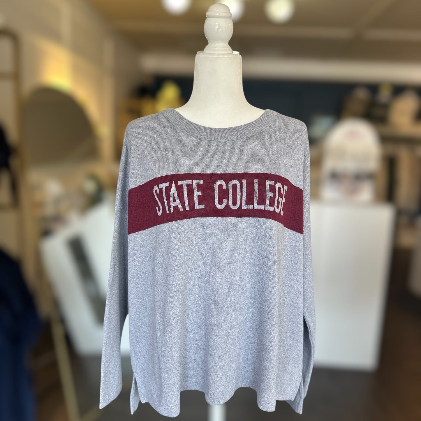 Gray sweater with 'STATE COLLEGE' text on a mannequin in an indoor setting.