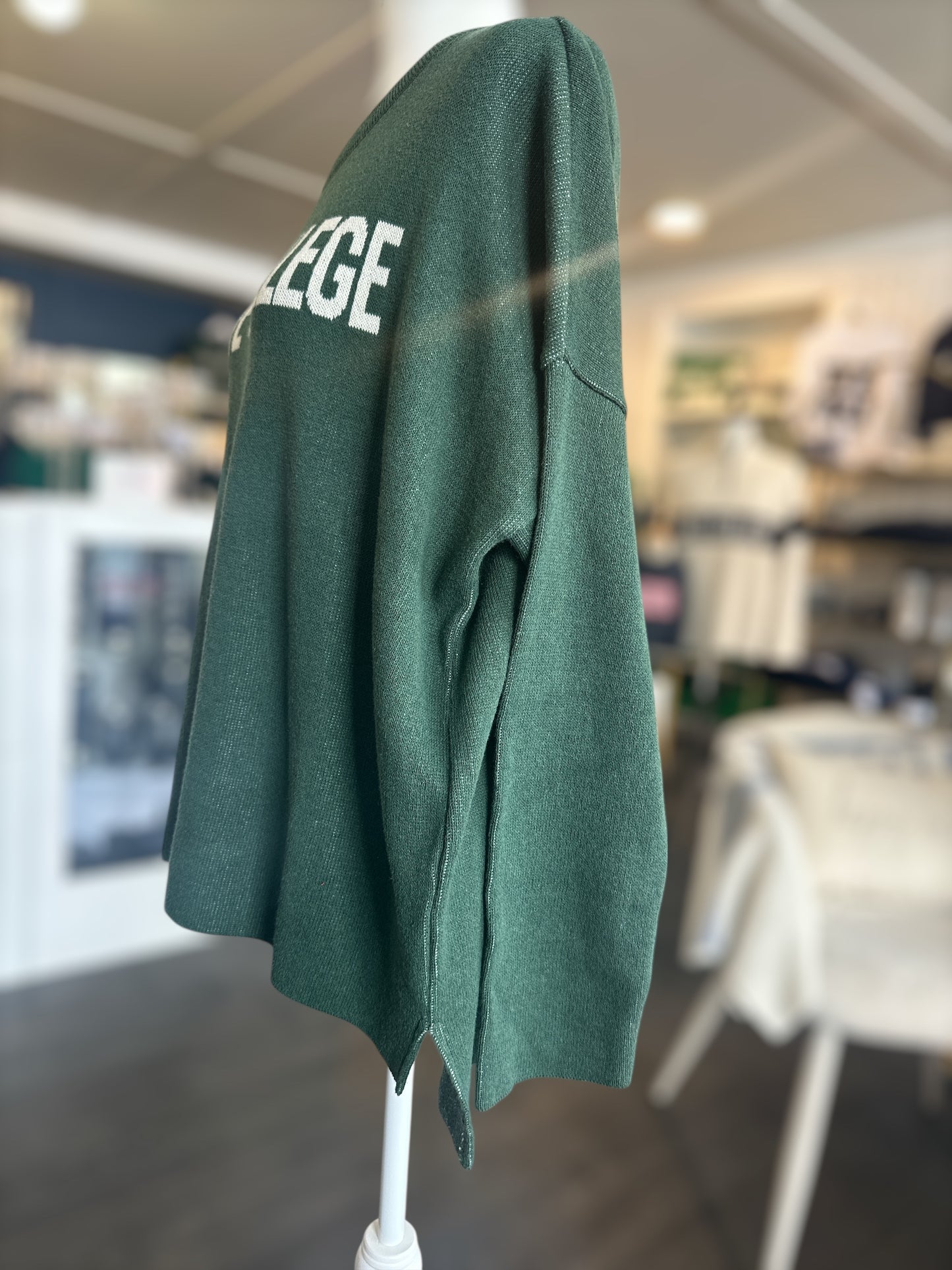 Green sweater with STATE COLLEGE' text on a mannequin in a store setting