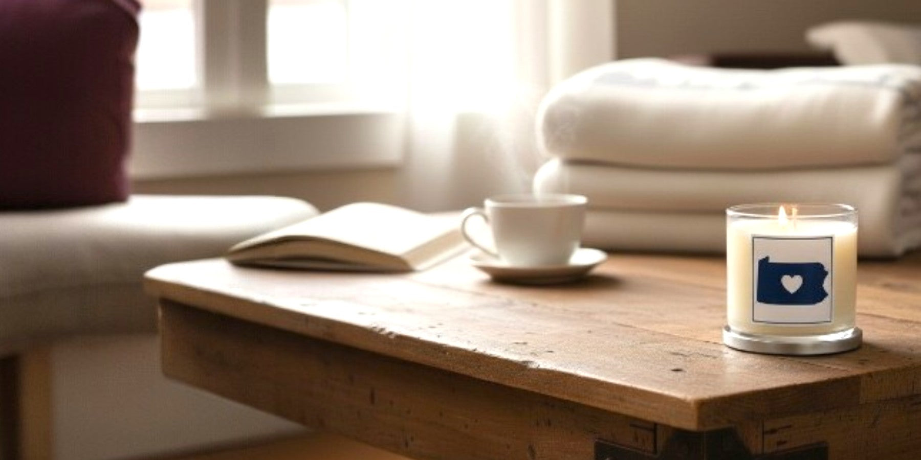 Candle with a heart and home icon on a wooden table in a cozy living room.