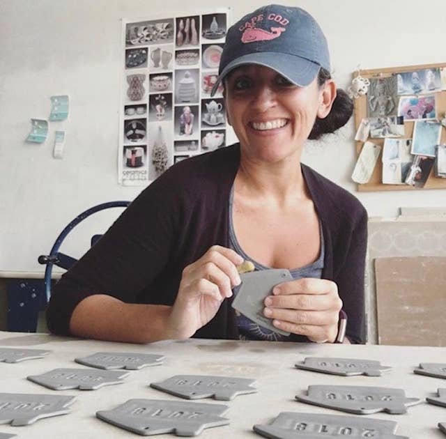 Woman wearing a cap, sitting at a table with ceramic items, in a workshop setting.