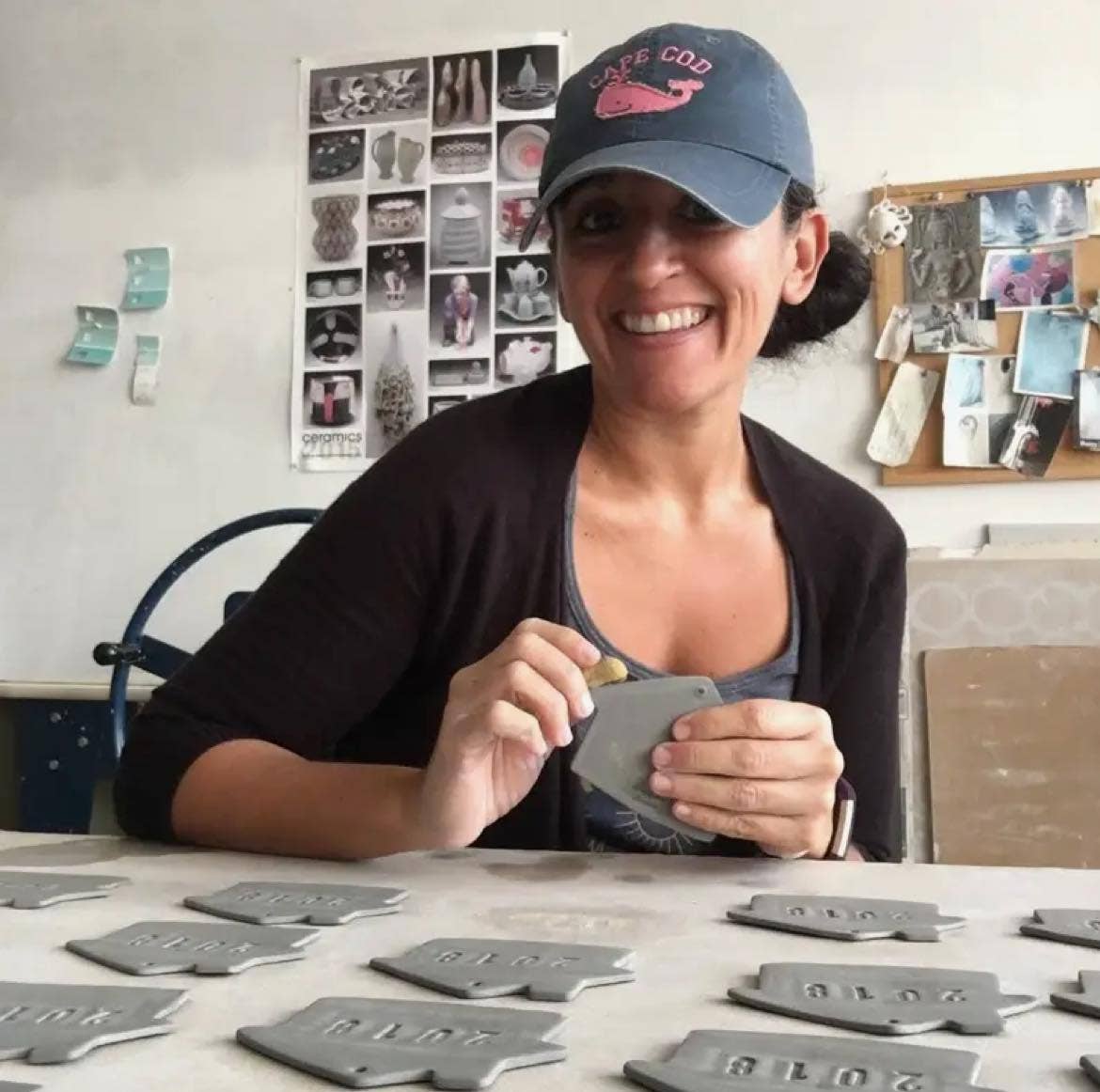 Woman wearing a cap and holding a metal tag in a workshop setting