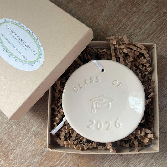 Ceramic disc with 'Class of 2026' engraving in a box with crinkled paper lining.