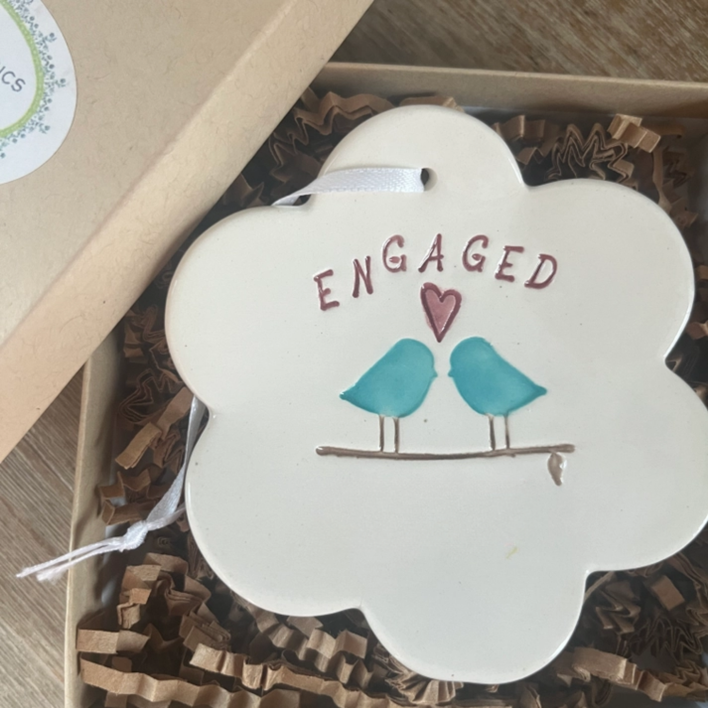 Decorative item with 'ENGAGED' text and two birds on a branch, placed in a box.