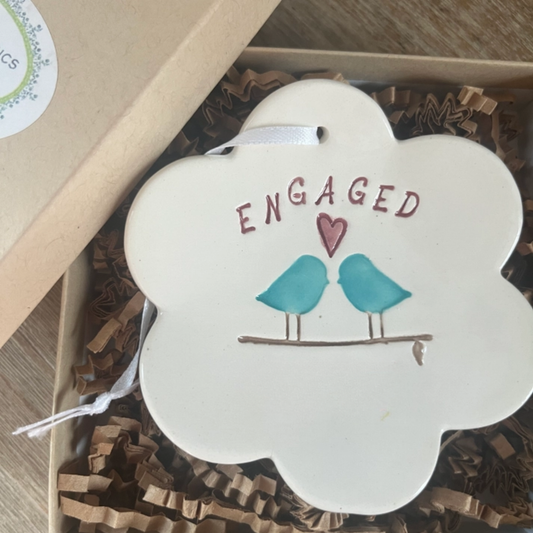 Decorative item with 'ENGAGED' text and two birds on a branch, placed in a box.