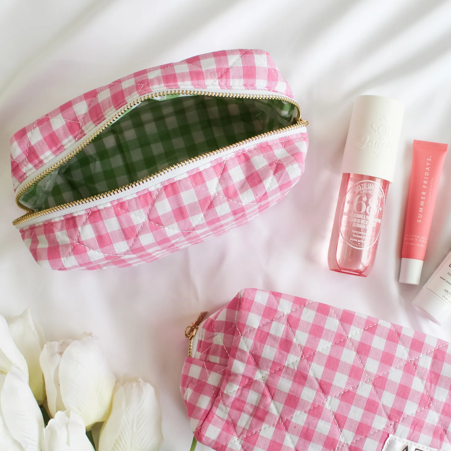 Pink gingham makeup bag with cosmetic products on a white background