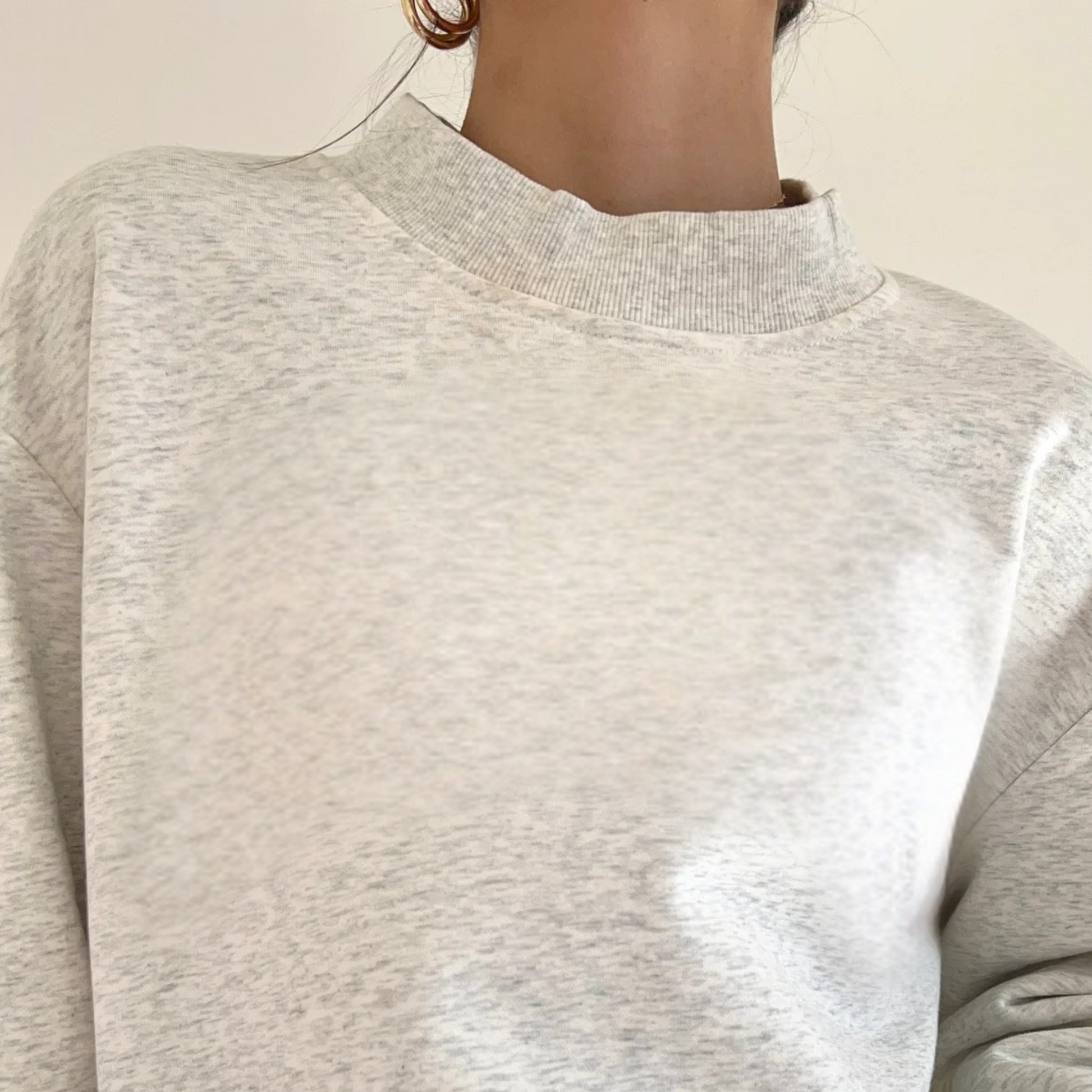 Close-up of a person wearing a light gray sweater against a neutral background