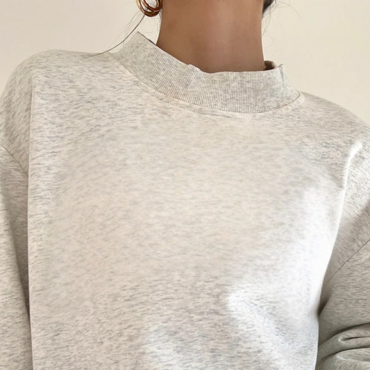Close-up of a person wearing a light gray sweater against a neutral background