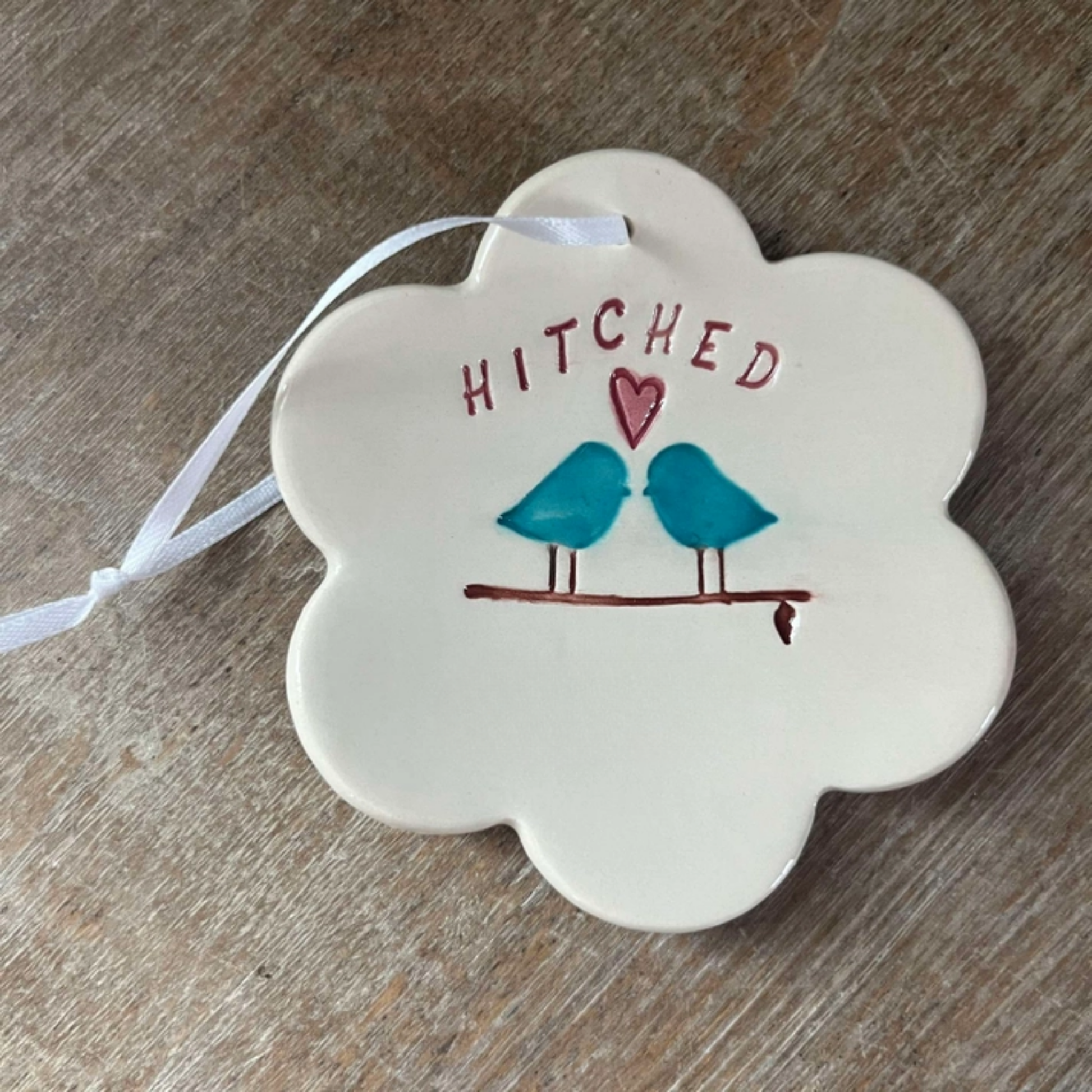 Decorative ornament with 'Hitched' text and bird illustration on a wooden surface