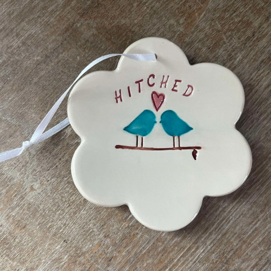 Decorative ornament with 'Hitched' text and bird illustration on a wooden surface
