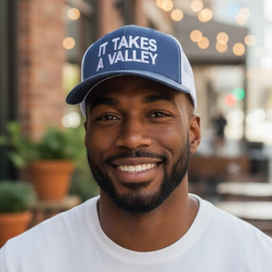 Man wearing a blue cap with 'It Takes a Valley' text, smiling outdoors.