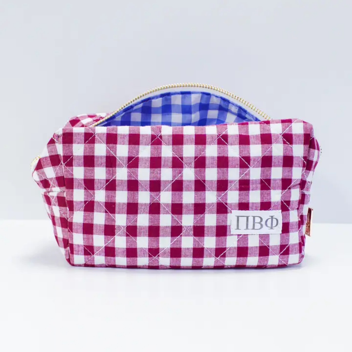 Quilted pouch with red and white checkered pattern and gold zipper on a light gray background