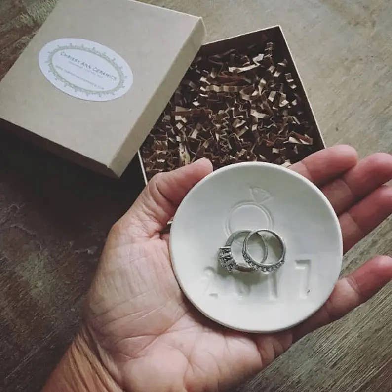 Hand holding a white dish with rings, with an open box of ribbons in the background.