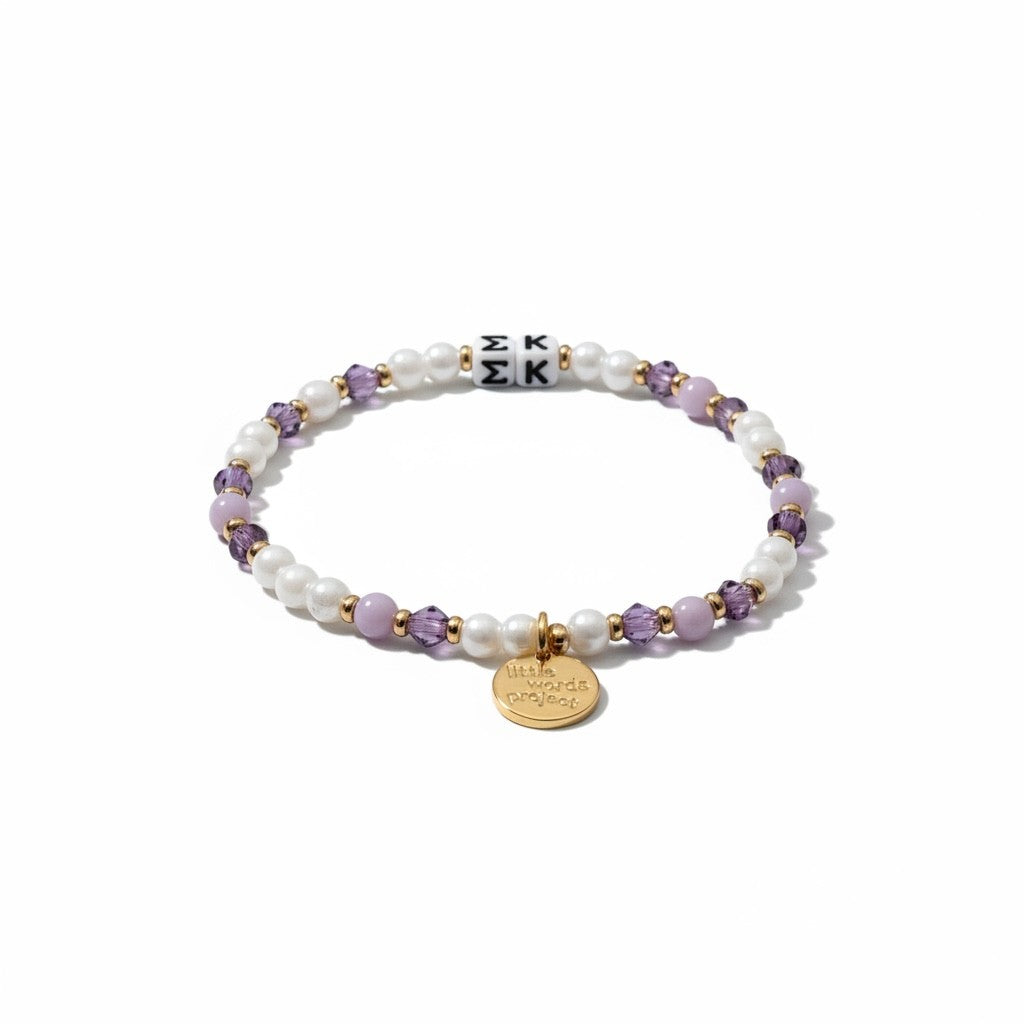 Bracelet with pearls, purple beads, and a gold tag on a white background