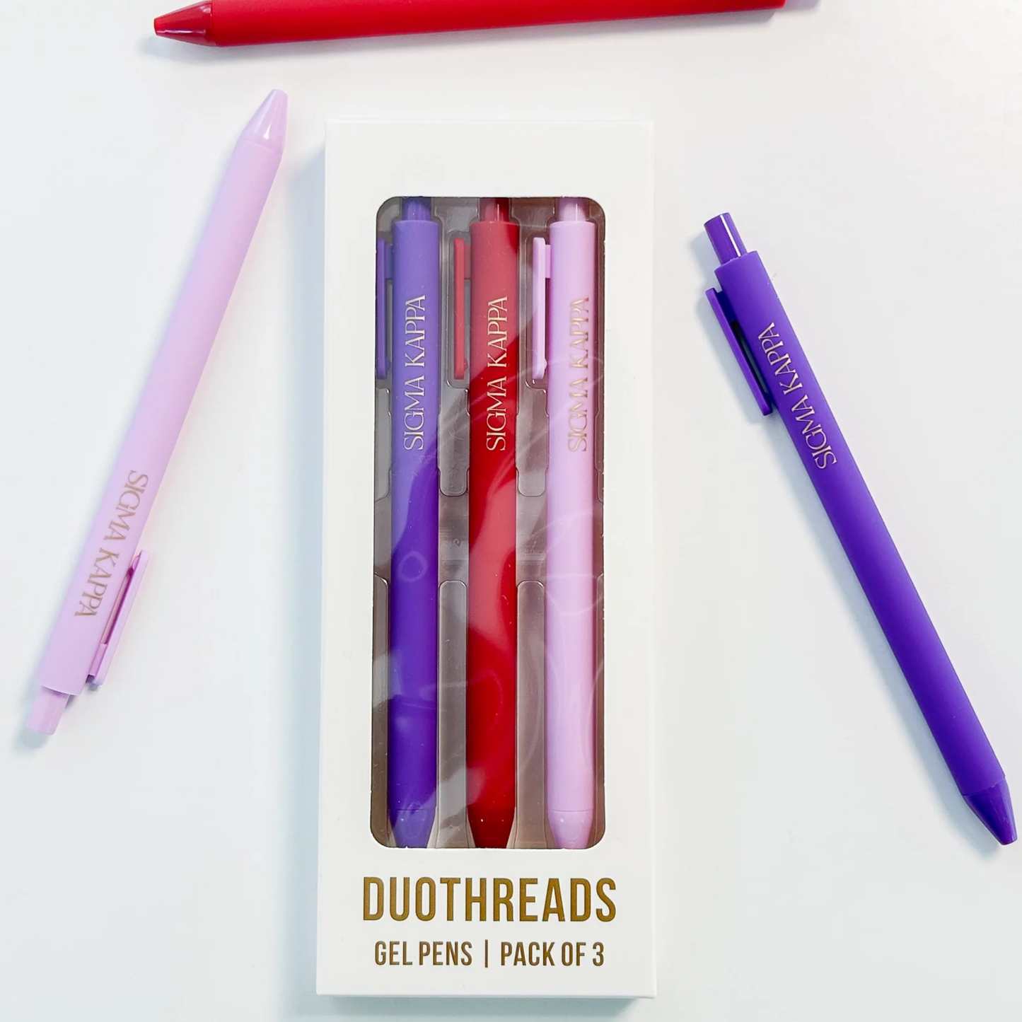 Set of three gel pens in purple, red, and pink with packaging on a white background
