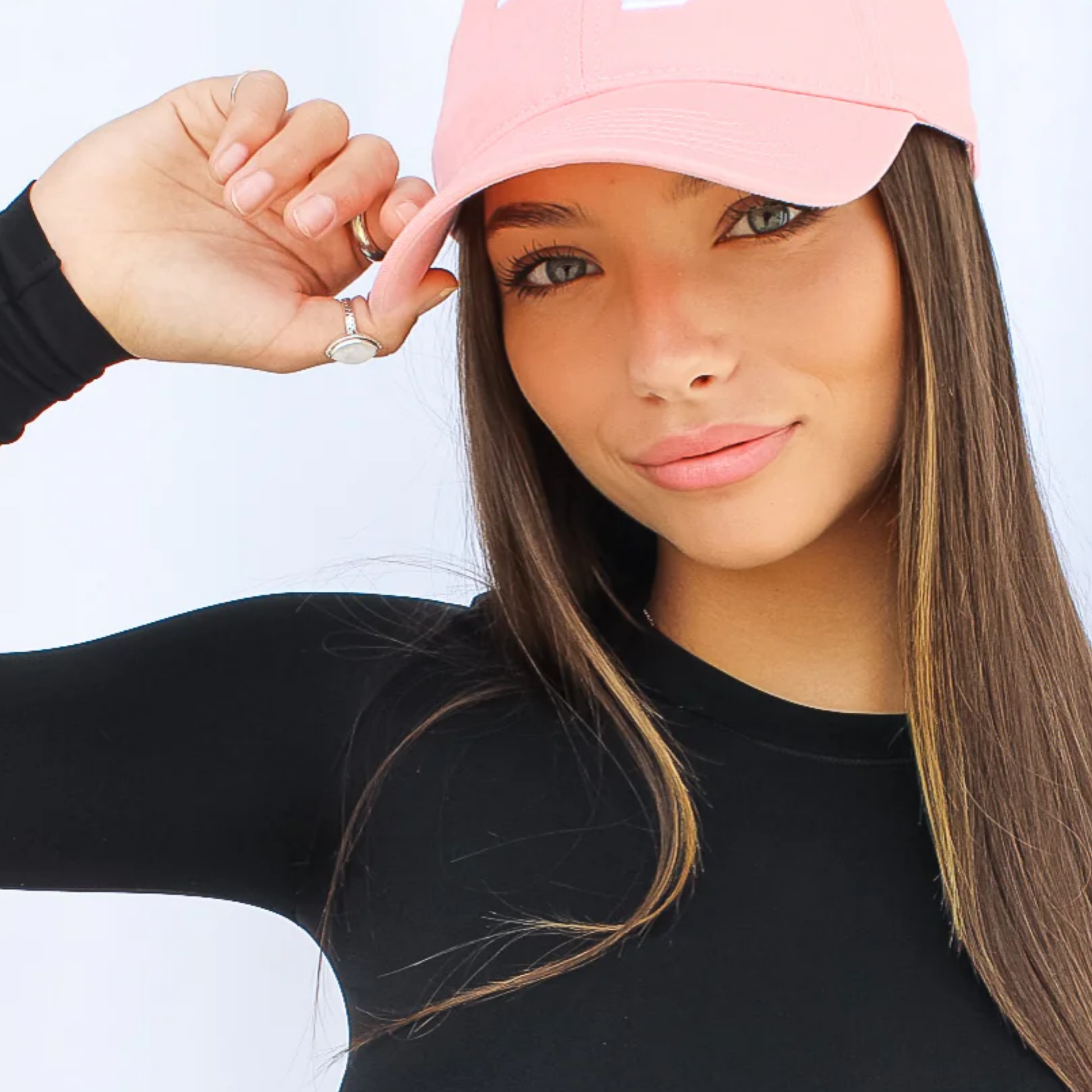 Woman wearing a pink cap and black long-sleeve shirt against a white background