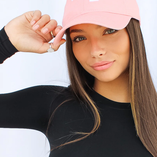 Woman wearing a pink cap and black long-sleeve shirt against a white background
