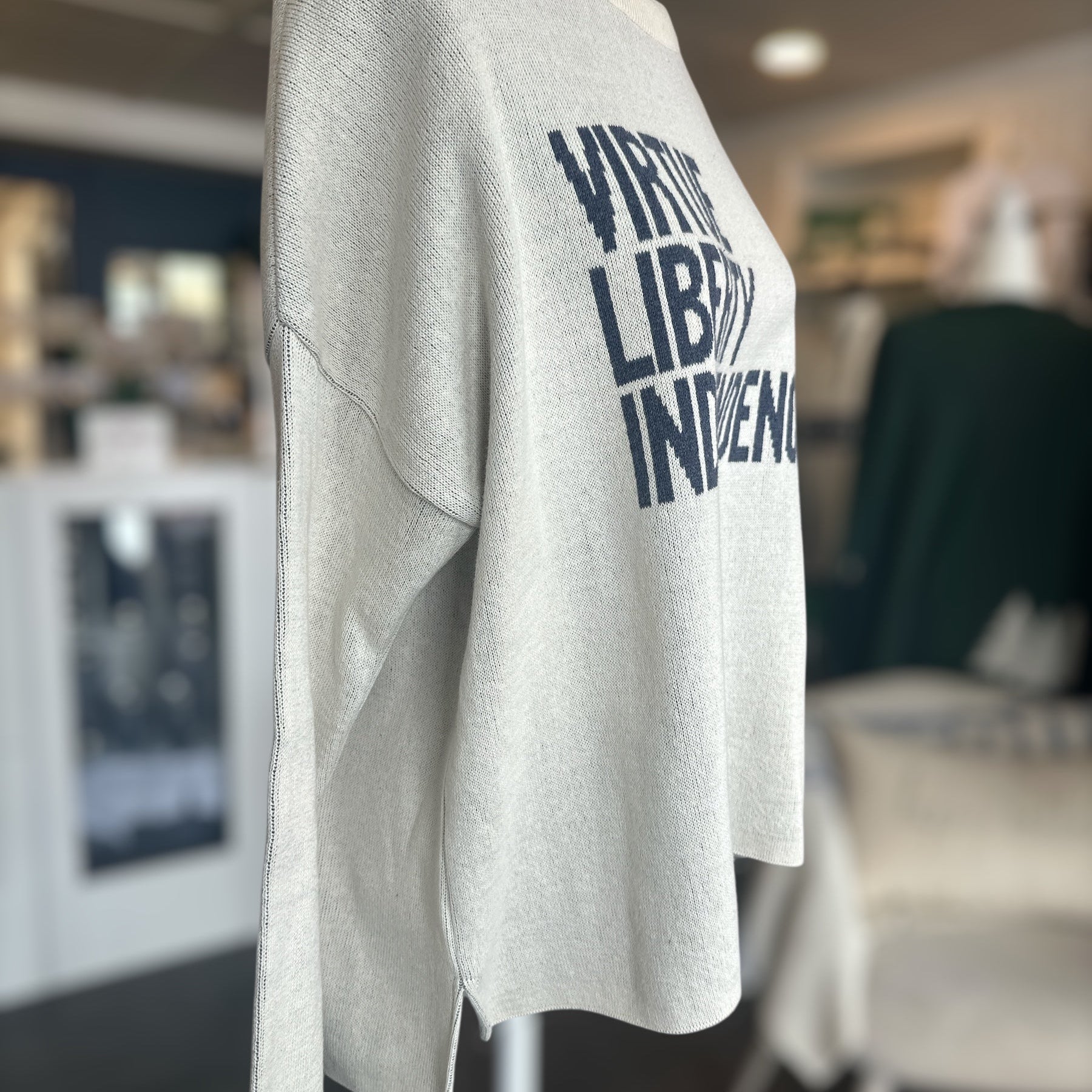 sweater with 'Virtue Liberty Independence' text on a mannequin in an indoor setting.