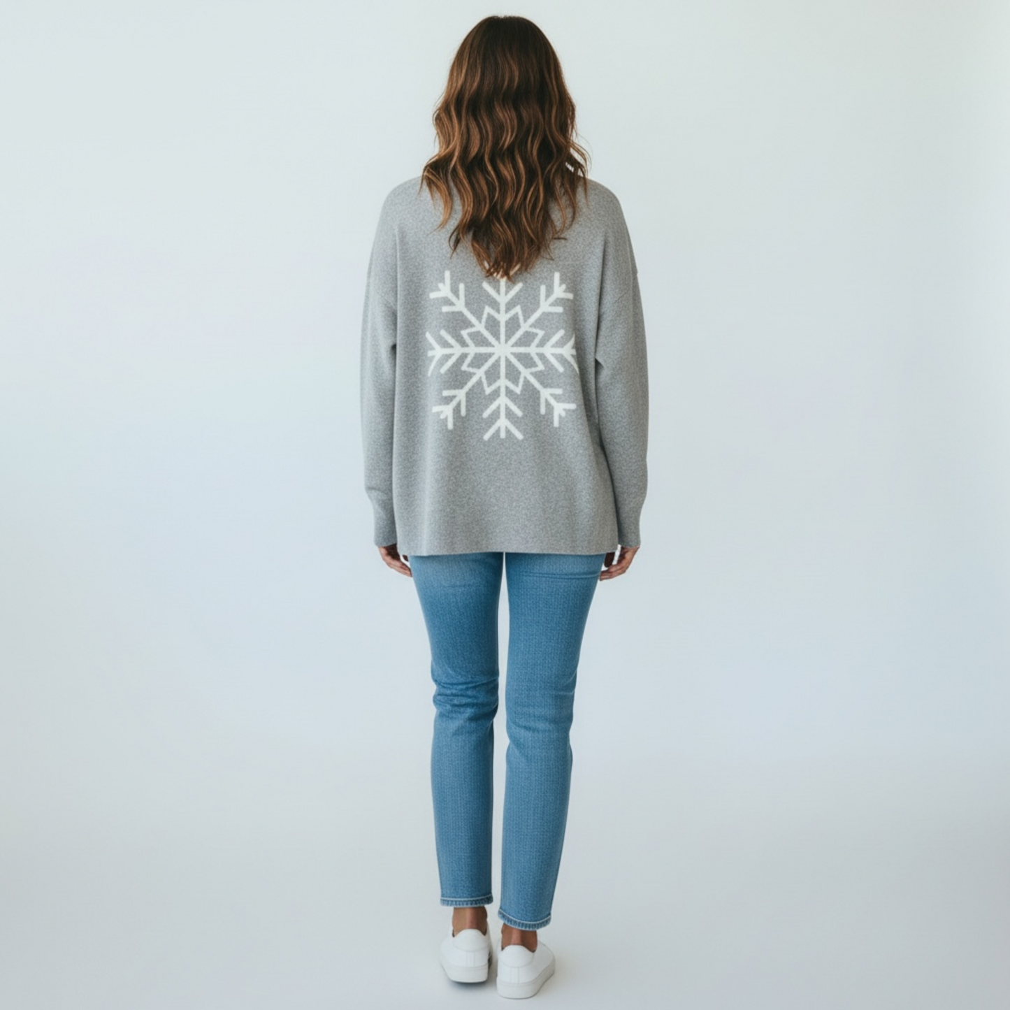 Person wearing a gray sweater with a snowflake design on the back, standing against a white background.