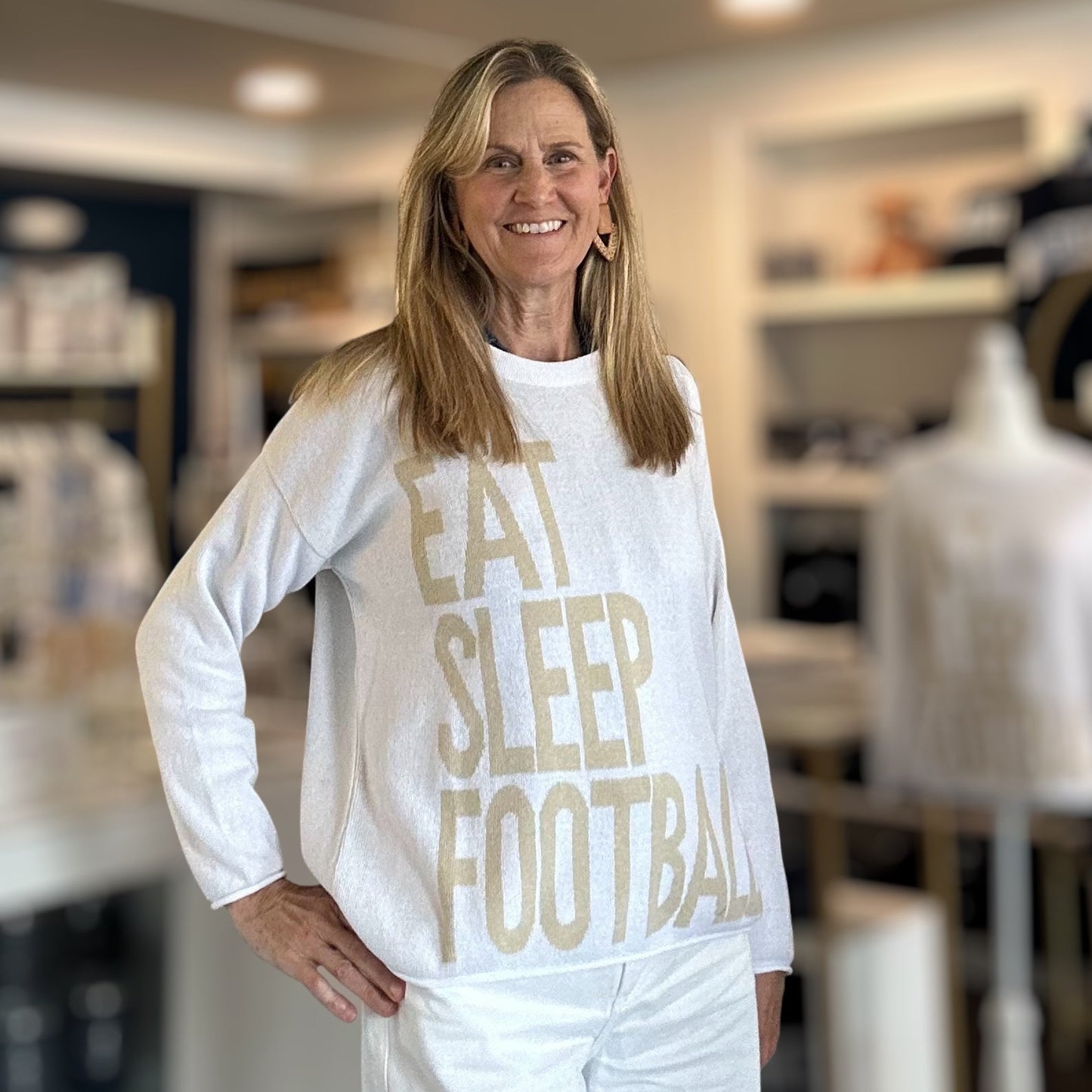 Woman wearing a white sweatshirt with 'EAT SLEEP FOOTBALL' in a store setting