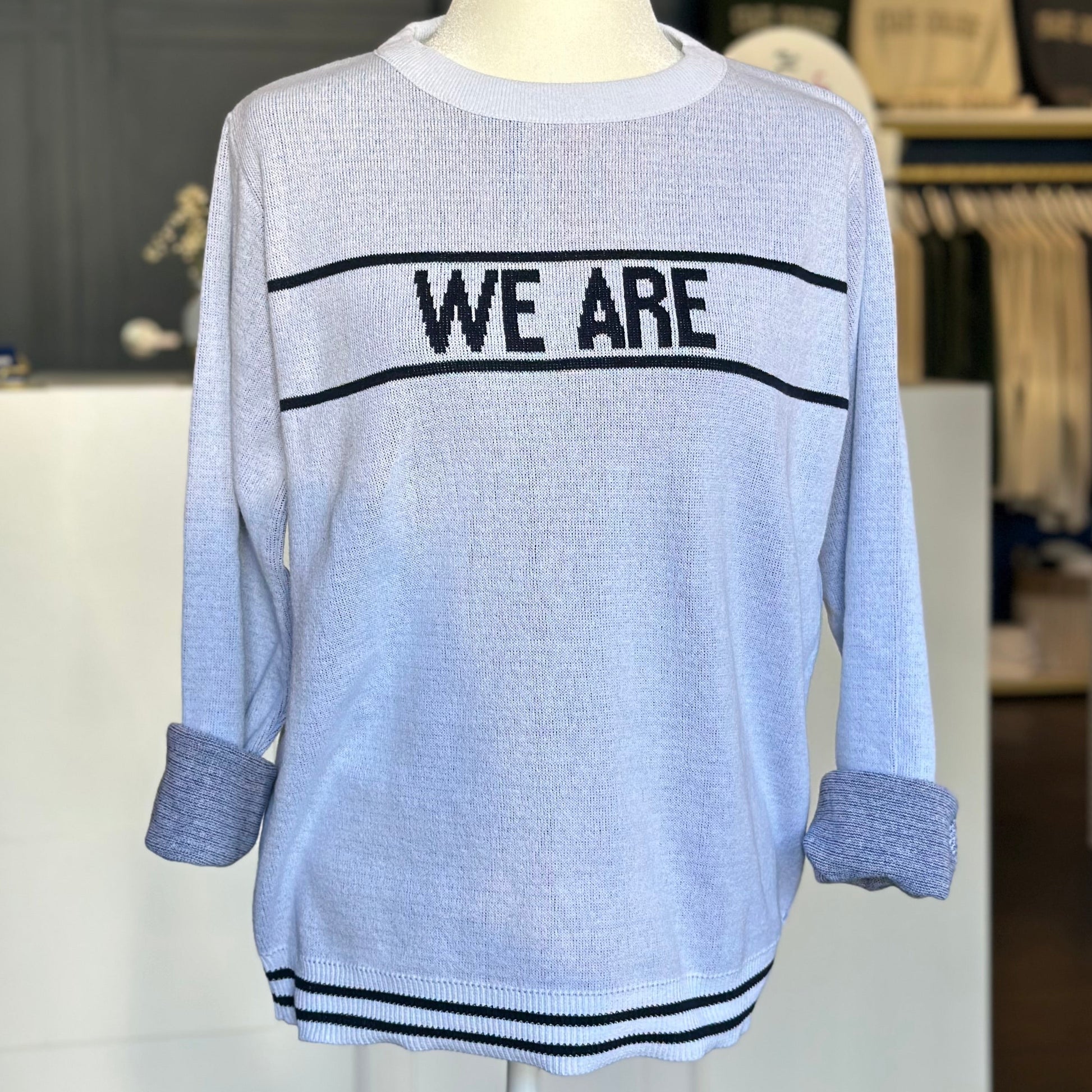 Light blue sweater with 'WE ARE' text on a mannequin in a store setting