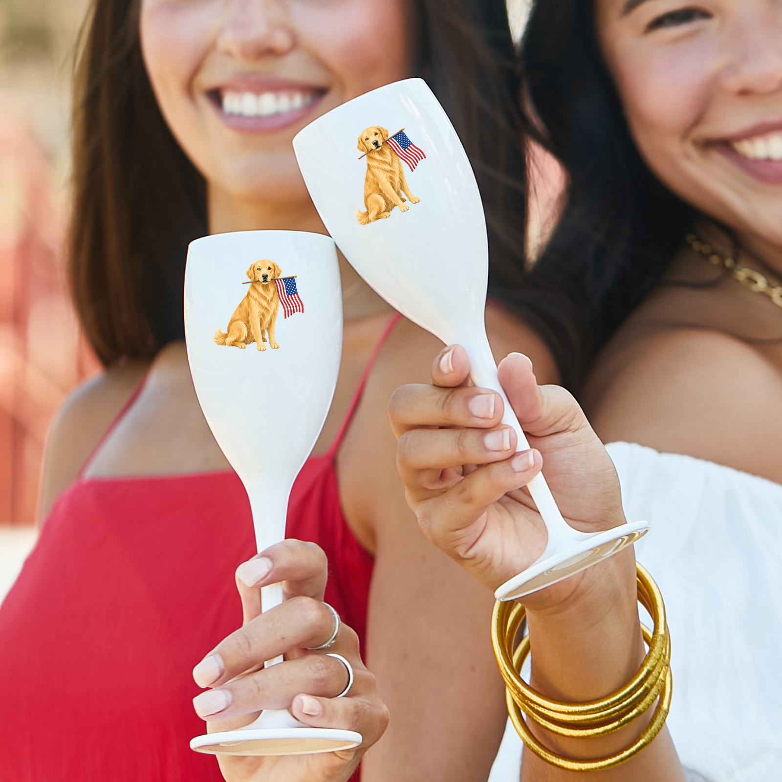 Two women holding white wine glasses with dog illustrations and American flags.