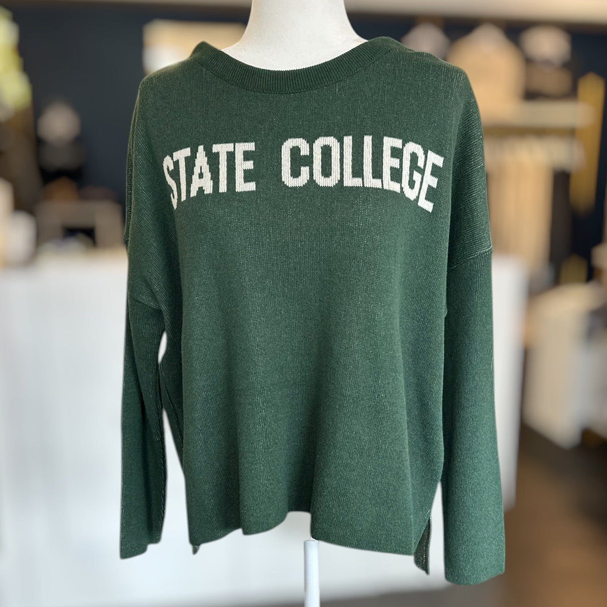 Green sweater with 'STATE COLLEGE' text on a mannequin in an indoor setting.