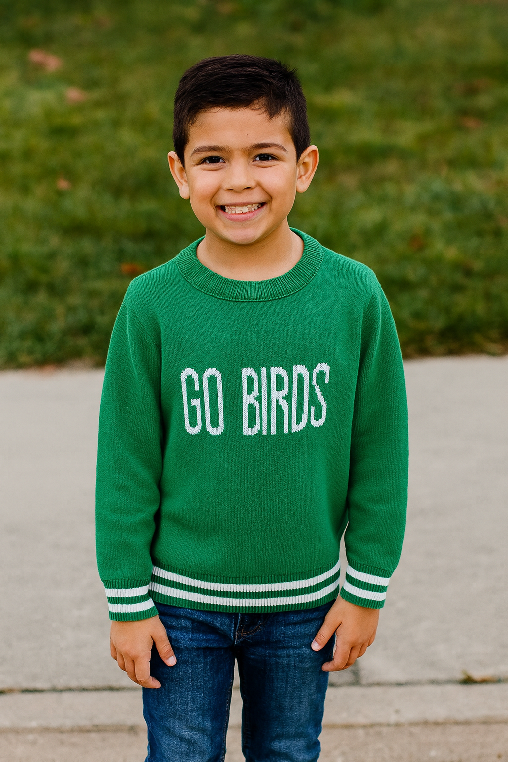 Child wearing a green sweater with 'GO BIRDS' text, standing outdoors.