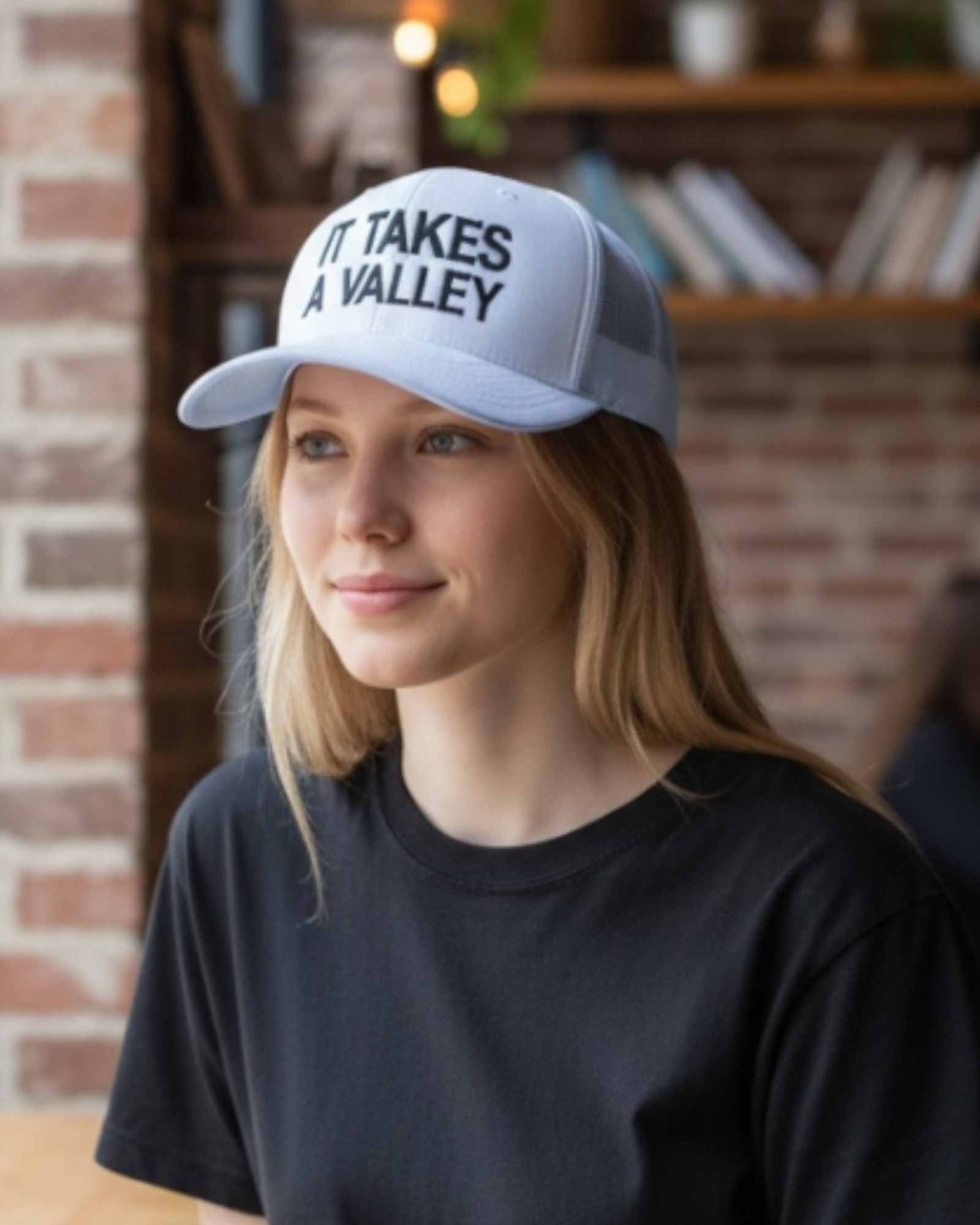 Woman wearing white It Takes A Valley™ trucker hat inside a local coffee shop, showing embroidered front panel. 2