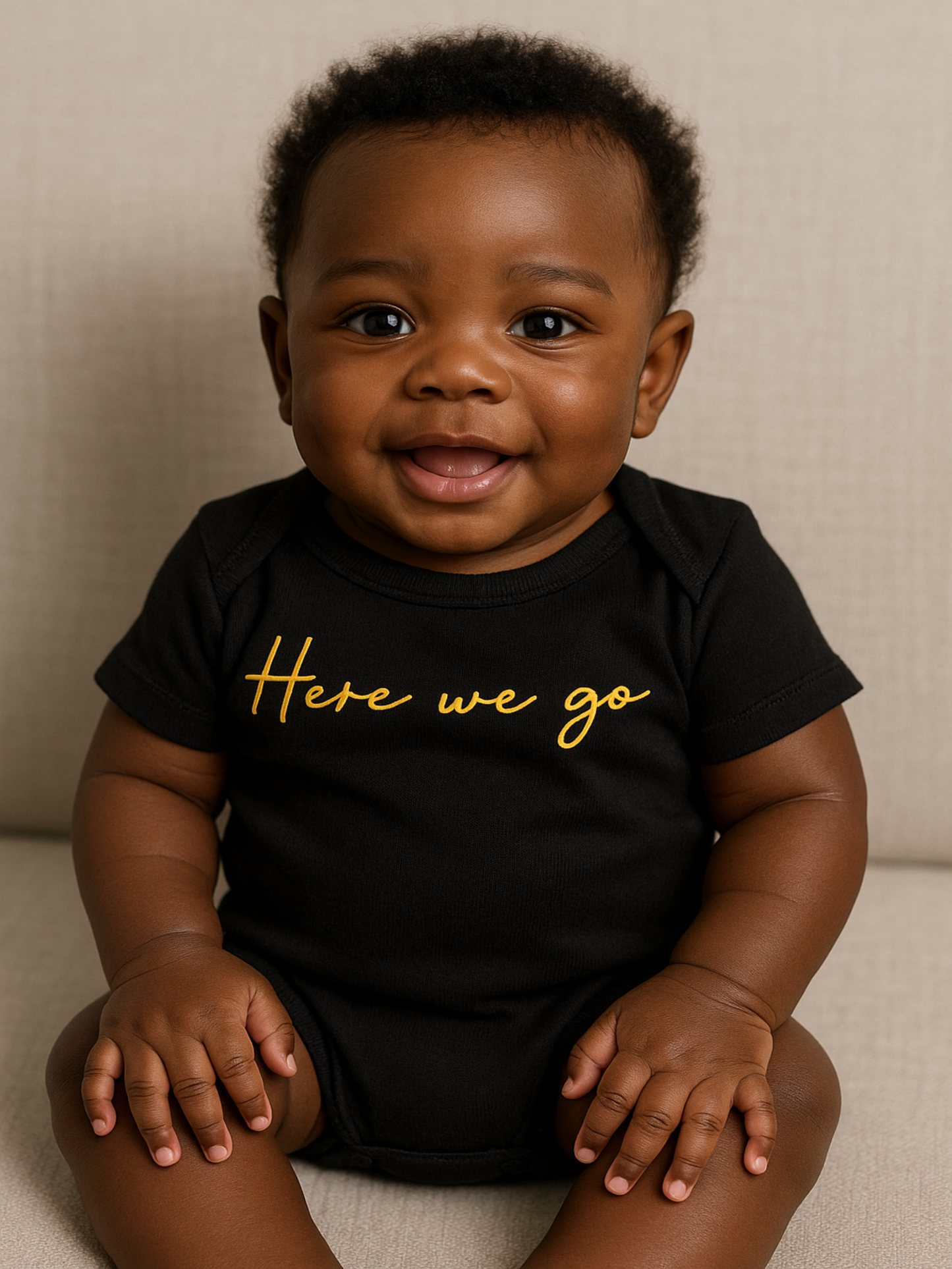 Smiling baby wearing Rabbit Skins® black and gold “Here We Go” onesie – Town Pride USA-printed baby bodysuit inspired by hometown pride.