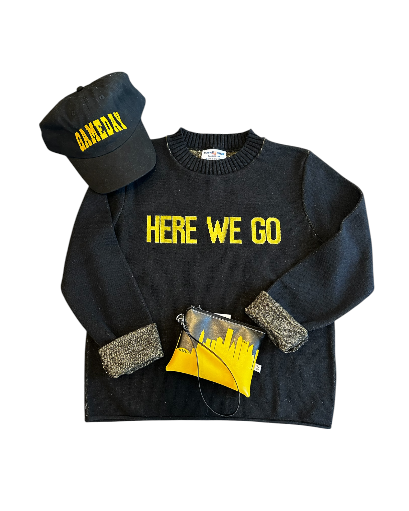 Flat lay of black “HERE WE GO” sweater with black gameday hat and gold Pittsburgh skyline wristlet, styled for game day.