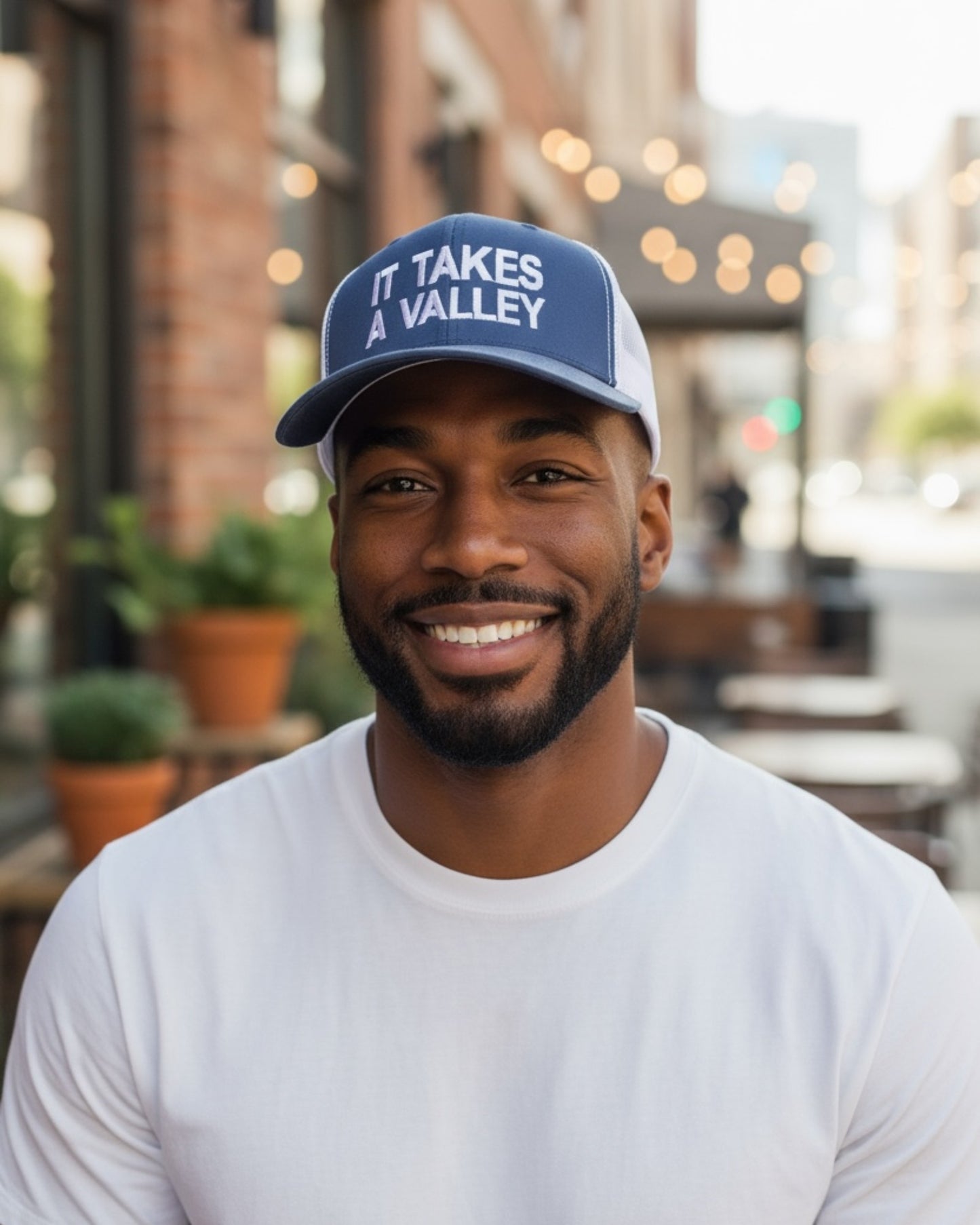 Man wearing navy and white It Takes A Valley™ trucker hat from Town Pride State College, photographed outdoors.