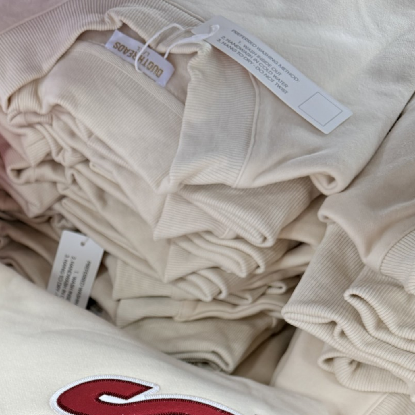 Stack of beige sweaters with tags on a white background