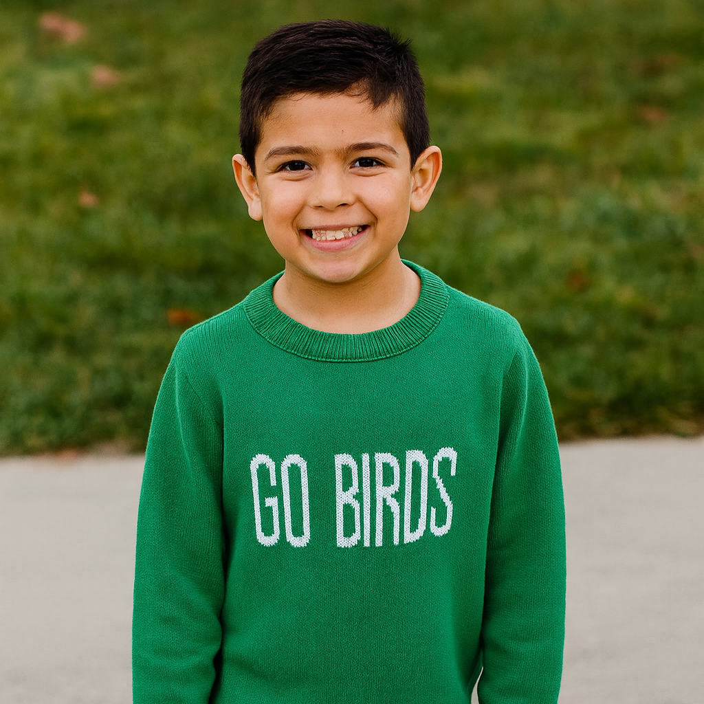 Child wearing a green sweater with 'GO BIRDS' text, standing outdoors.