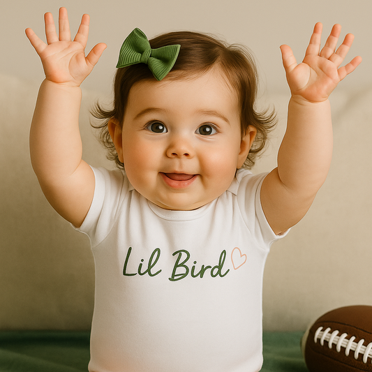 Baby wearing a 'Lil Bird' onesie with arms raised on a green blanket.