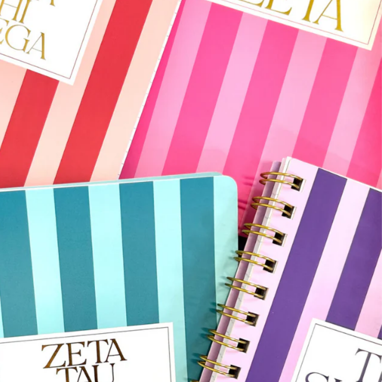 Three spiral-bound notebooks with colorful striped designs and visible text on a white background.