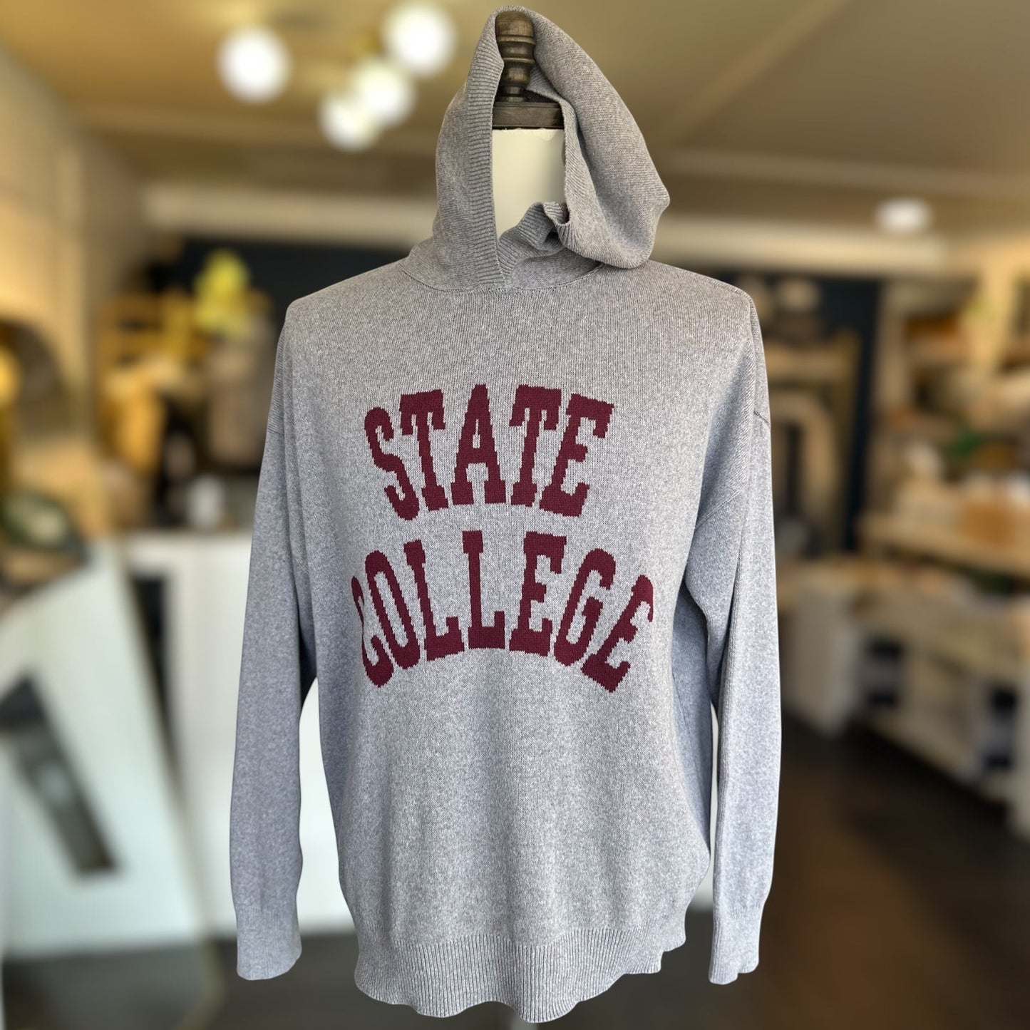 Gray hoodie with 'STATE COLLEGE' printed in red on a mannequin in an indoor setting.