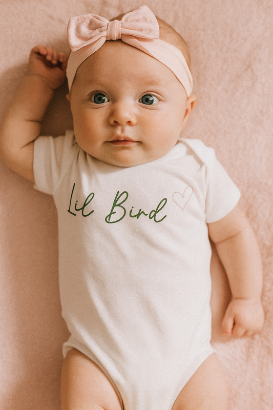 Baby wearing a 'Lil Bird' onesie and pink headband on a soft pink background