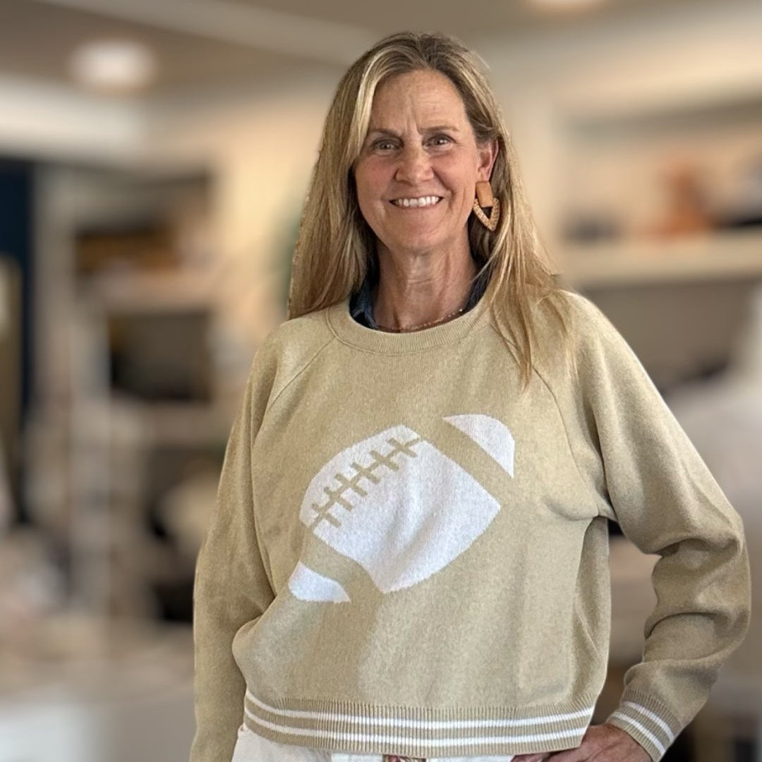 Woman wearing a beige sweater with a white graphic design, standing indoors.