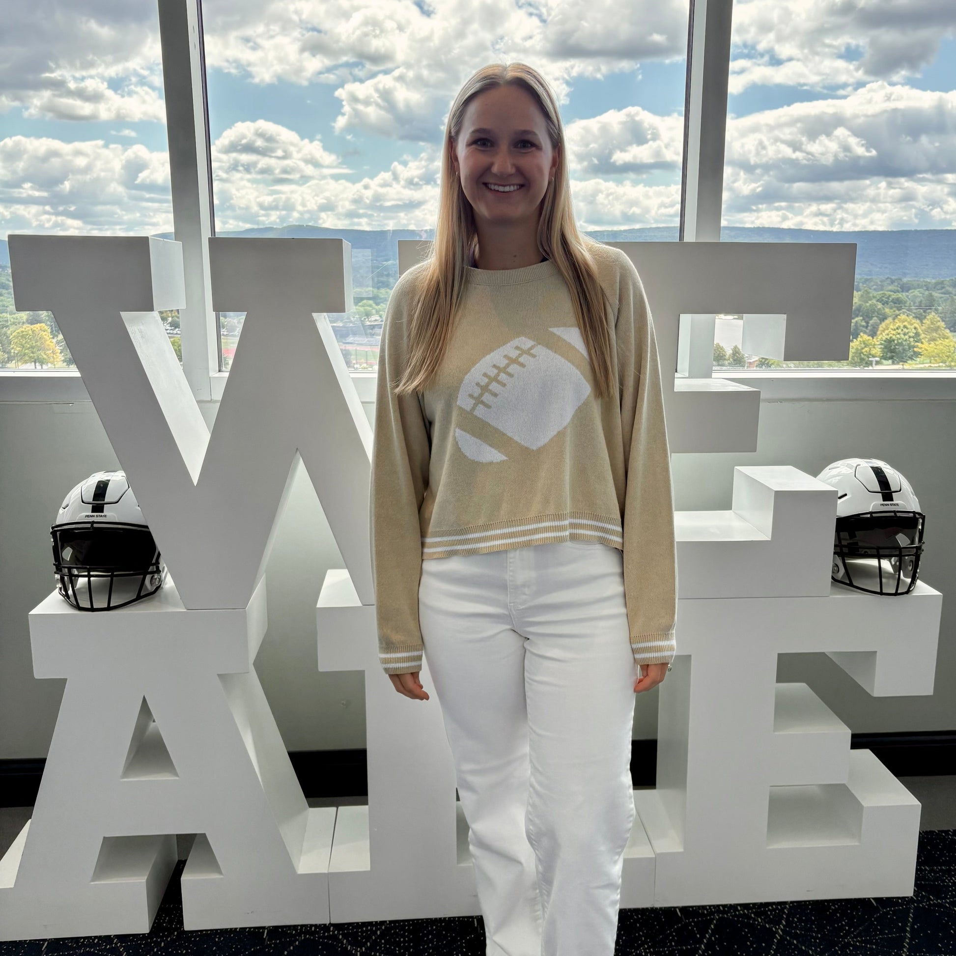 Person standing in front of large white letters spelling 'WE ARE' with a scenic background.