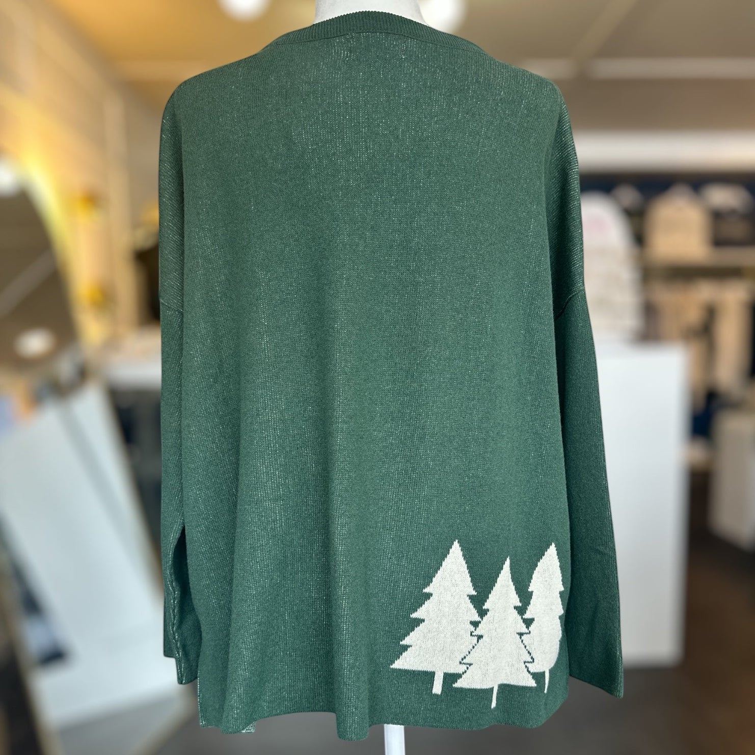Green sweater with white tree designs on a mannequin in a store setting