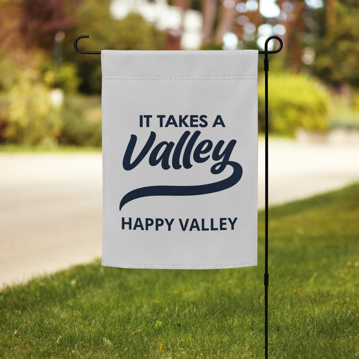 Town Pride State College Happy Valley garden flag with navy text on a white polyester background in a yard.