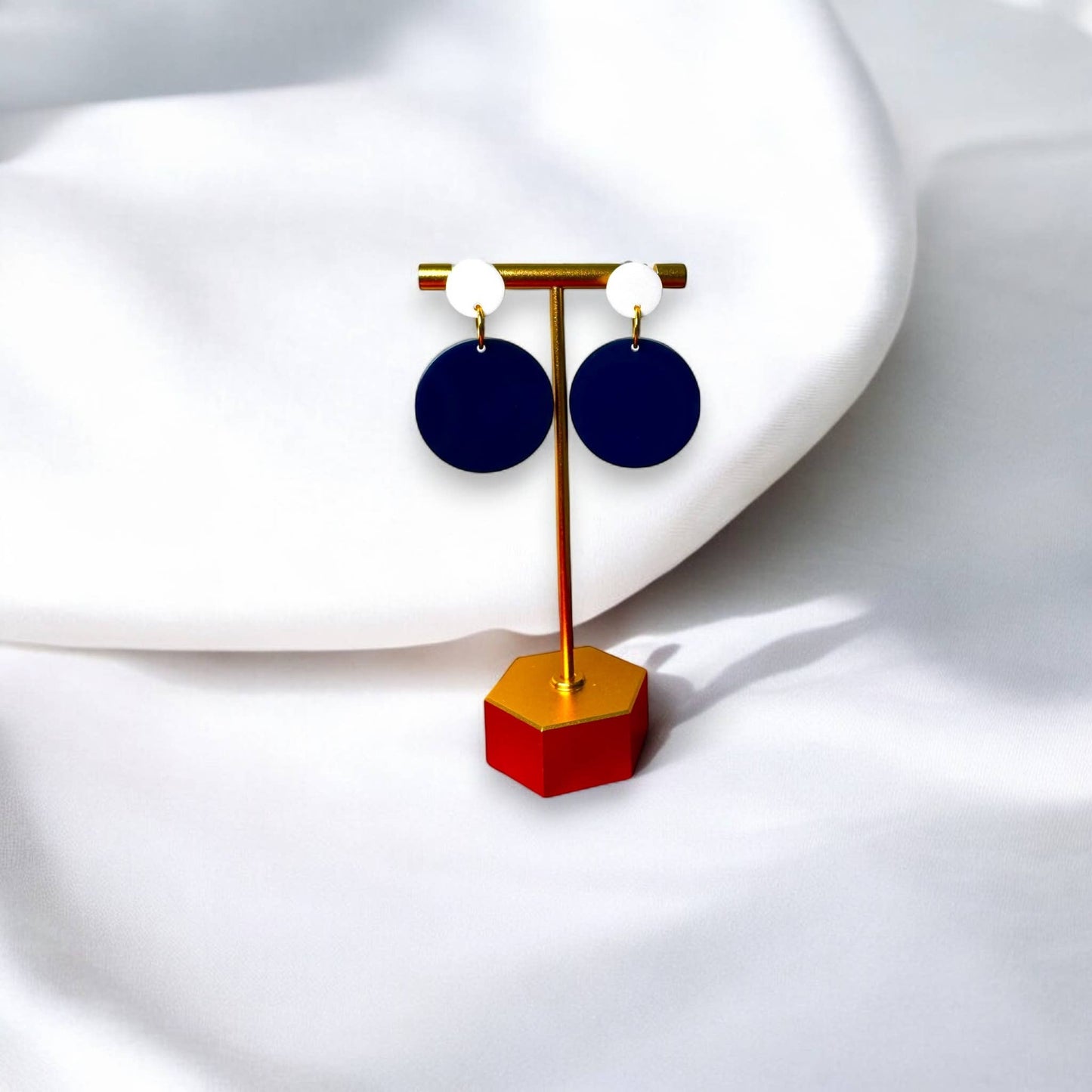 Town Pride State College navy blue and white circle acrylic earrings on a gold display stand against white fabric.